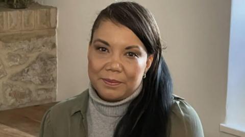 A woman with dark brown hair and a brown coat. 