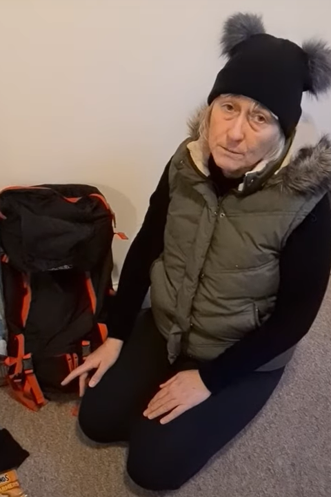 Amanda Evans kneeling next to her rucksack, wearing a bobble hat and gilet