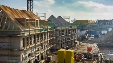 Scaffolding surrounds dozens of properties being built on an estate which has building paraphernalia scattered about as construction work is carried out