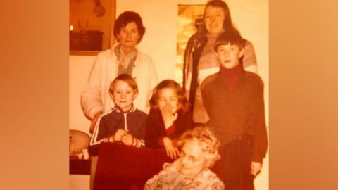 Pictured in this sepia image sitting in the armchair is May Stephan (the great-grandmother), behind the armchair (l-r) are Peter, Mary and Richard (the great-grandchildren) and behind Richard is his mother, Alison, and behind Peter is the grandmother, Marjorie.