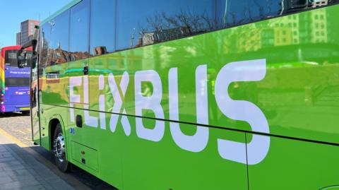 A bright green coach is parked up at a bus stop, with 'FLIXBUS' in white writing down the side of it.