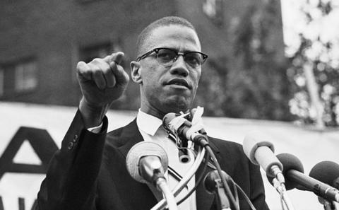 malcolm x speaking into microphones during a  rally in the US