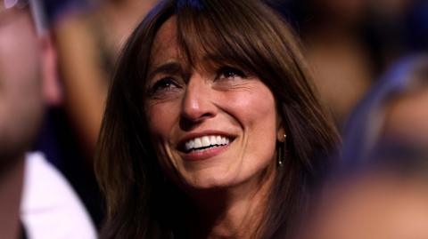 Davina McCall looking up at the stage at the National Television Awards in September 2024. She has her long brown hair down and is smiling.
