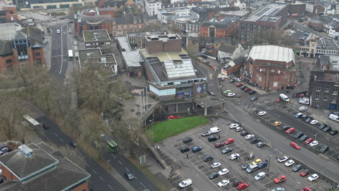 Ariel view of Swindon town centre. There are multiple building in the background, roads and two car parks. Both car parks have multiple cars parked in bays. 