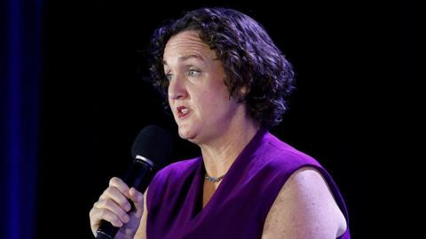 Katie Porter, wearing a purple top, speaks into a microphone