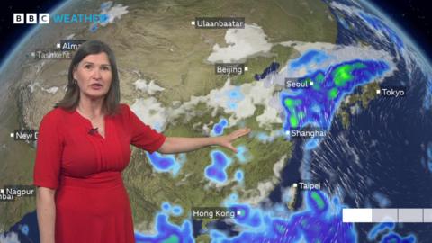 Helen Willetts in front of a tv Weather map showing heavy rain in eastern Asia