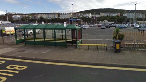 Cars parked in the empty lot behind a row of bus shelters and benches.
