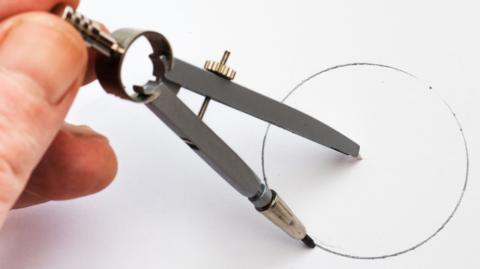 A picture of a hand using a compass drawing out a circle.