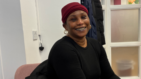 Sohna is smiling at the camera and is wearing a black jumper and a red hat.