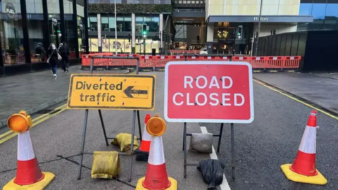 Road repair works under way with signs stating "road closed" and "diverted traffic", alongside three cones.