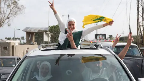 eople show victory signs from a vehicle as displaced people cross the bridge linking southern Lebanon