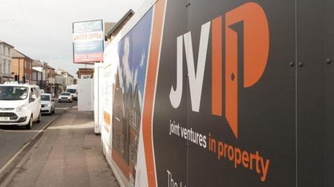 A wall sign that reads 'JVIP'. There are cars on the adjacent road. 