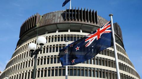 The New Zealand flag flies in front of its government building, known as the Beehive