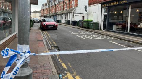 Police tape is stretched across a residential street. 