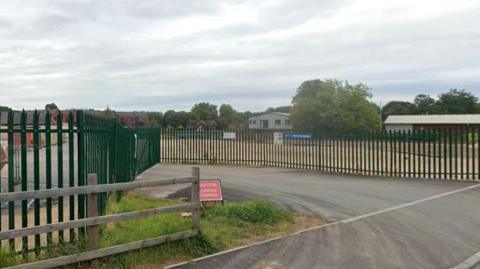 A green metal fence dividing a road and driveway from the open land behind it