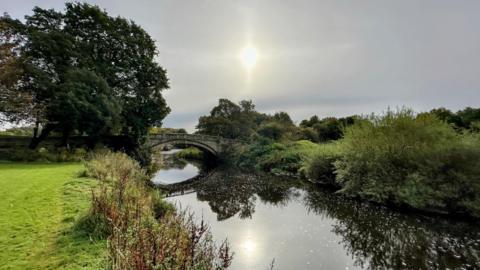 A grey, cloudy sky above a small river with a stone bridge.
