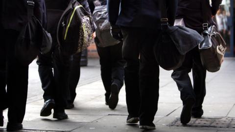 Behind a group of young people walking with school bags. 