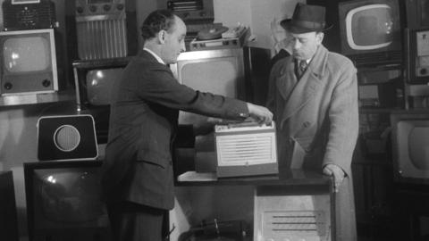 Two men surrounded by televisions and radio sets.