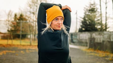 A female jogger stretches her arms in the city park