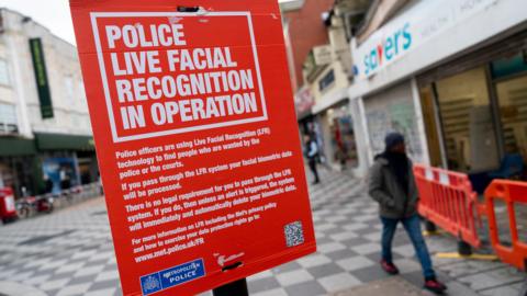 A red sign fixed to a lamppost explaining the Metropolitan Police was deploying the use of live facial recognition technology in Croydon, south London, on Friday February 9, 2024. A QR code is on the bottom right corner of the sign which members of the public could scan for more information. The bottom left corner of the sign features the Metropolitan Police insignia.