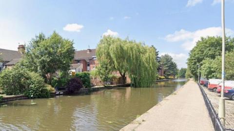 Canal towpath running past trees in a built up area