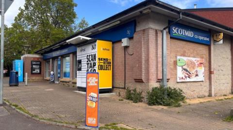 A street view of a shop on a residential street with trees behind