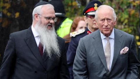 Rabbi Daniel Walker, with a long white beard and glasses, speaks to King Charles III, who wears a grey suit with a pink pocket square