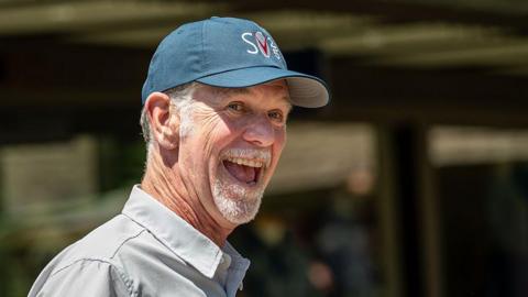 The co-founder of Netflix, Reed Hastings, wearing a blue baseball cap and grinning widely. 