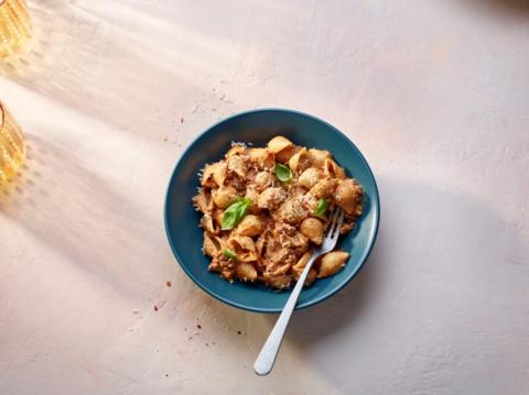 Beef and mascarpone pasta with green basil in a blue bowl with a fork