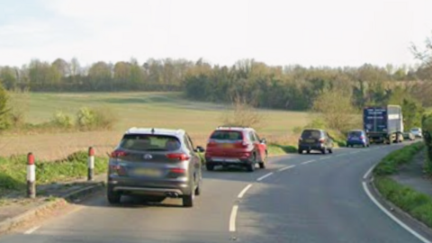A rural road with a queue of cars on it.