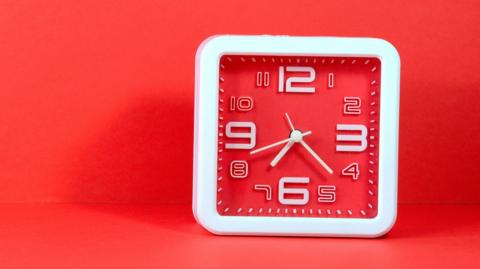 An red and white square-shaped analogue wall clock 