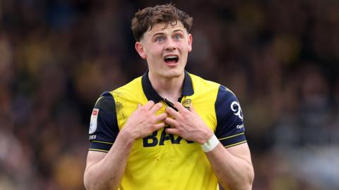 An image of Will Lankshear, wearing his yellow Oxford United home kit, gesturing towards himself during a match against Hull City in April