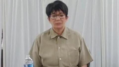Ghislaine Maxwell sits in a tan shirt with a water visible in front of her.