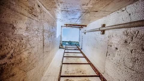 A concrete tunnel with steps leading towards an entrance at the top. 