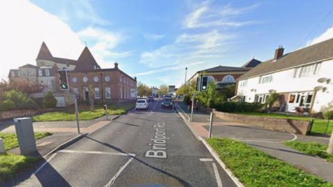 Road with traffic lights and crossing - traffic can be seen in the distance and buildings are on with side.