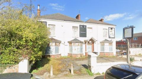 Streetview image of large derelict pub building with boarded up windows
