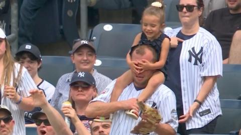 A small girl sitting on a man's shoulders covers his eyes as he catches a ball