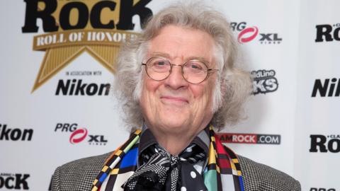A man with grey hair and glasses is smiling at the camera. 
