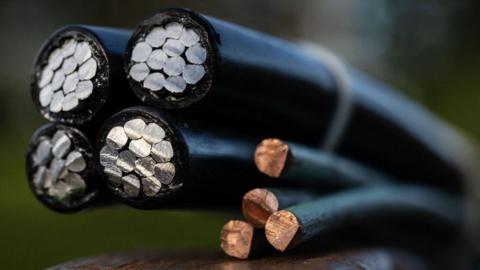 A close up of a cut section through four multi-core steel wires and four copper wires, all coated in black.