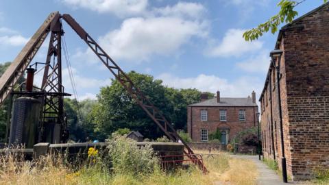 A piece of industrial heritage machinery, with a redbrick building in the foreground.
