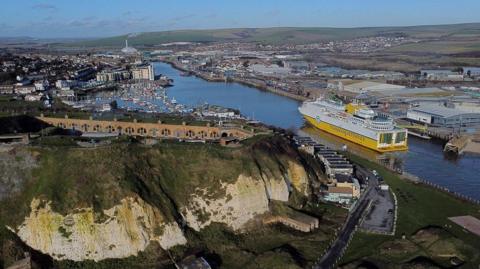 The East Sussex town of Newhaven, from the air. A white ferry with a yellow hull is moving through the port towards the town centre.