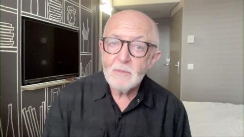 Jeremy Bowen, wearing glases ,looks to camera