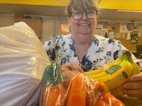 A woman wearing glasses, with a bag of food including bananas and carrots