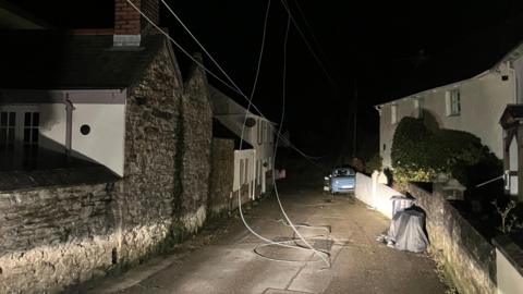A village street in the darkness, phone lines lie across the carriageway following a storm.