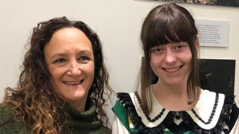 Photographer Gillian Allard and 16 year-old Amelie stand by a photography display of portraits and colourful nature images.