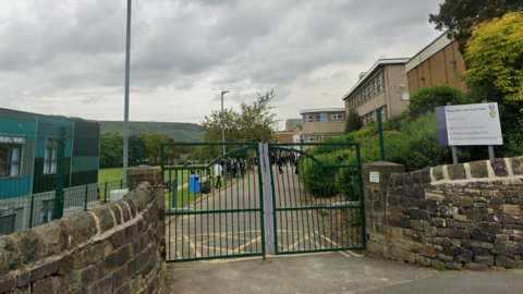 A school building built on a slipe with a sign for the building and black gates