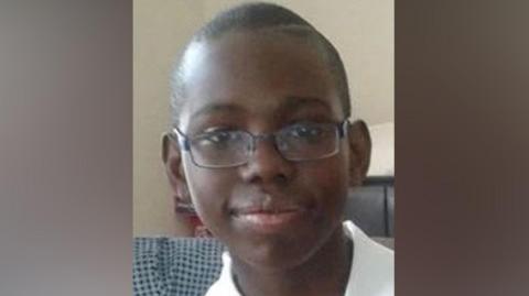 A teenage boy with very short hair and wearing glasses