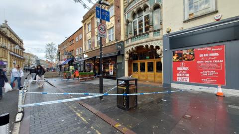 Police tape on the pavement outside the Turkey Cafe with members of the public having to divert around the scene.