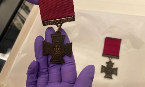 A person wearing purple gloves holding a  Victoria Cross medal