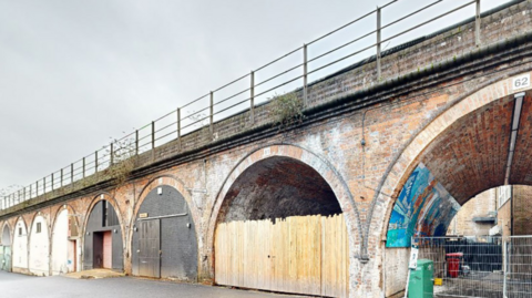 A series of railway arches. Some are boarded up, others are bricked up and other have metal fencing to prevent access.